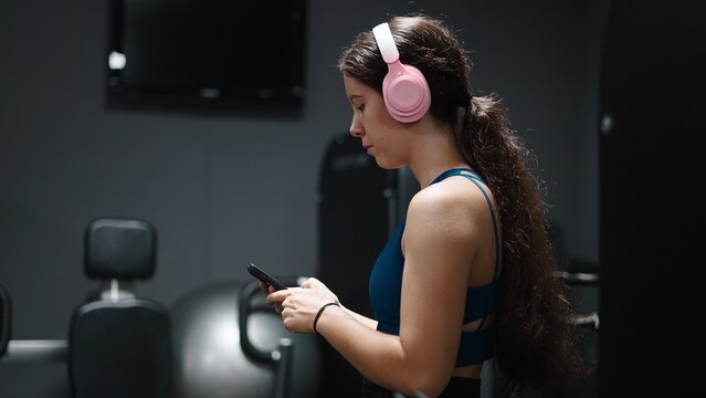 Young woman using smartphone and listening to music with headphones in gym