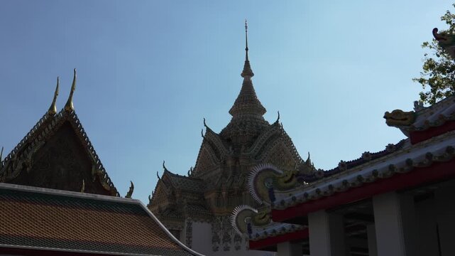 Daylight view of richly adorned rooftops, central spire, and naga finials at Wat Pho, the Temple of the Reclining Buddha, located south of the Grand Palace in Rattanakosin, Bangkok, Thailand