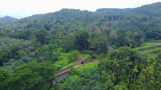 Aerial view of an historic stone bridge aqueduct and elevated road traversing a dense tropical valley, with betel nut areca palm plantations climbing the surrounding forested hills.