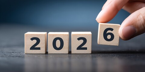 Wooden blocks displaying the year 2026 with a hand placing the last block, creating the new year, concept for new year resolutions, business forecasting and financial planning