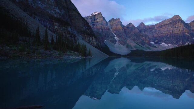 Moraine Lake darkens at twilight as soft blue light settles over calm water and sharp peaks of Valley of Ten Peaks reflect clearly creating quiet alpine mood in still mountain scene.