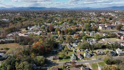 Residential area of American town with colored leaves of trees in autumn. Aerial backwards wide shot. Streets and roads in suburbia of USA. Sunny day and mountains in distance.