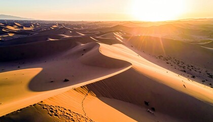 Vast desert landscape with rolling sand dunes bathed in the warm glow of a setting sun, casting long shadows and creating dramatic light.