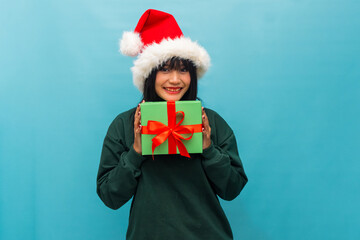 Cheerful Asian woman in Santa hat holds a Christmas gift smiling Ideal for holiday promotions and festive greetings