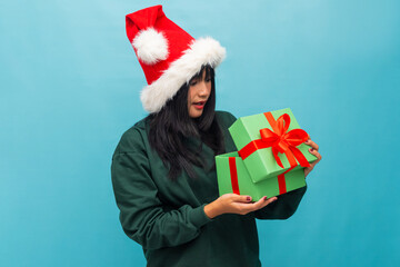 Playful woman in Santa hat examines gift box curiously Ideal for Christmas unboxing and festive promotional content