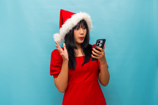 Happy woman in Santa hat uses phone while smiling Ideal for Christmas greetings and online celebration visuals - Powered by Adobe