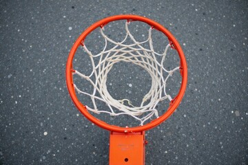 Close up of a weathered basketball on a cracked court with a blurred hoop. A close up, detailed shot of a weathered, scuffed orange basketball resting on cracked asphalt of an outdoor basketball