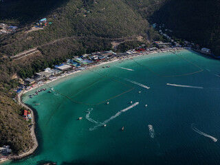 Stunning high-angle aerial drone view of Tawaen Beach on Koh Larn (Coral Island), Pattaya, Thailand. The image captures the crescent-shaped white sand beach, vibrant turquoise and emerald green waters