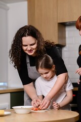Mother and daughter bond by cooking together in kitchen. Woman helps girl chop vegetables and teaches how to make salad. Cooking together as family. Teaching daughter culinary skills, hobbies.