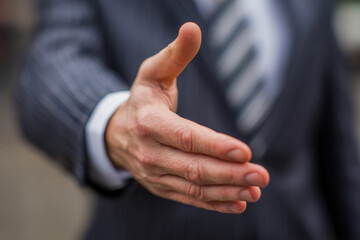 Business professional offering a handshake gesture in a striped suit and tie symbolizing greeting, agreement, partnership, and trust in a corporate setting