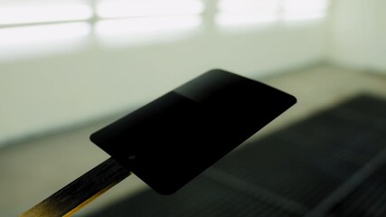 Professional auto body technician applies black paint onto a small test panel using a spray gun inside a clean, well lit automotive paint booth. - Powered by Adobe