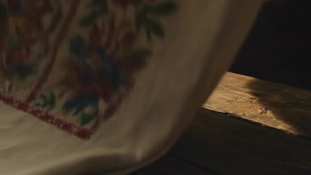 Hands lay out embroidered floral fabric on a rustic wooden surface