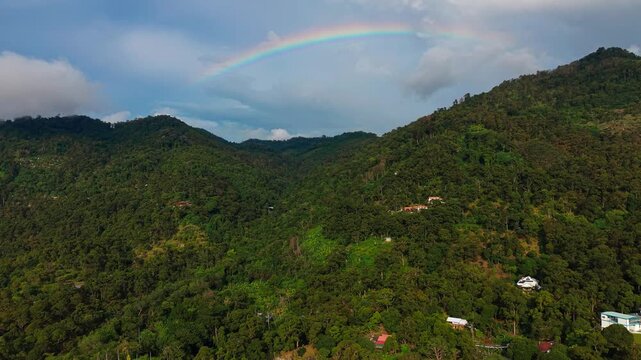 Spectacular Aerial Drone Shot of Double Rainbow Arching Over Lush Green Mountain Landscape After Rainfall