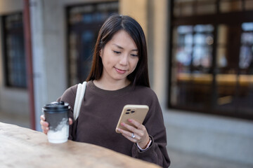 Woman holding coffee cup while using phone outside in city