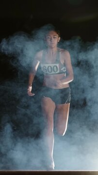 female athlete running from darkness through fog vertical slow motion fullHD symbol of strength motivation determination confidence victory mindset focus inspiration empowerment