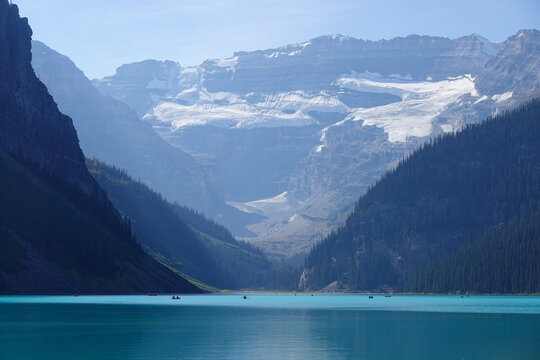 Boats crossing glassy turquoise lake beneath snowy peaks