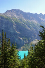 Turquoise lake beneath sunlit mountain wall and evergreen trees