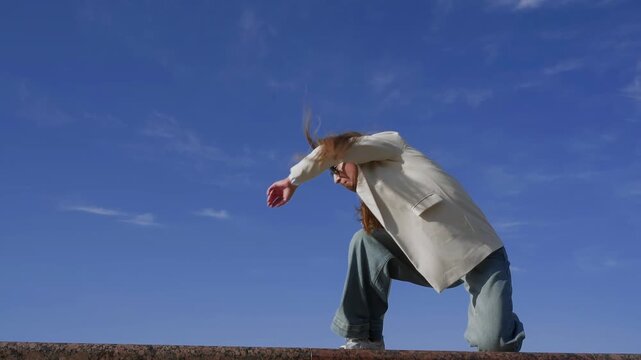 Stylish dancer in casual jeans, light blazer, and white T-shirt dancing contemporary modern dace moves expressively outdoors on stone surface, showing confidence and freedom in bright sunlight.