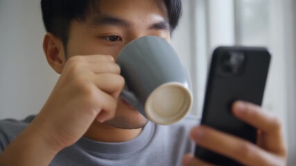 A young man enjoying coffee while using a smartphone.
