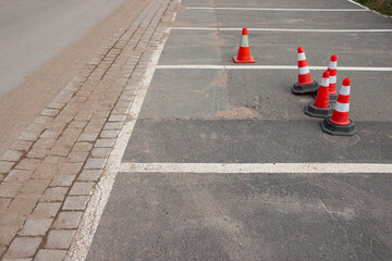 Traffic cones positioned on an empty parking lot, with clear lines and a smooth asphalt surface, creating a structured and organized environment for vehicle management