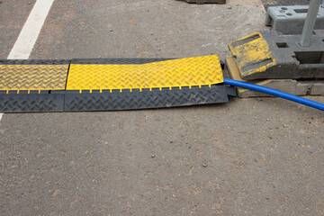 Yellow and black cable protector mat placed on asphalt surface, covering electrical cable, ensuring safety in construction area, preventing tripping hazards and damage to equipment