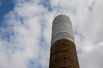 Tall industrial chimney wrapped in protective covering against a backdrop of cloudy sky, showcasing construction maintenance and urban architecture in a dynamic environment