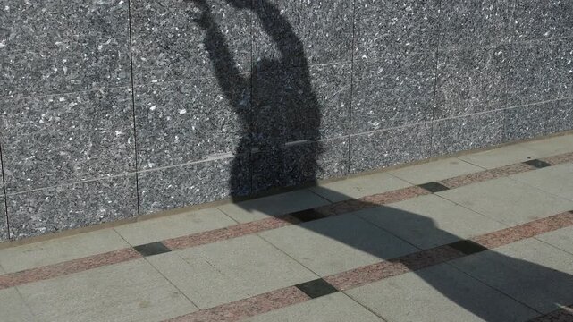 Long shadow silhouette of dancing woman dancing contemporary modern dace falls on gray tiled street, highlighting urban presence and sunny weather, shot without visible people.