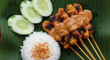 Delicious Sate Ayam with Peanut Sauce, Rice, and Fresh Cucumber on a Banana Leaf Plate
