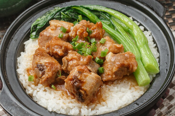 The braised pork ribs and kale rice, served in a black clay pot, was arranged on a tablecloth.