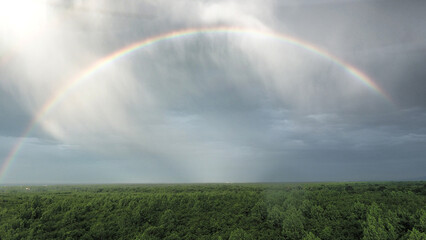 Aerial view of a rainbow arcing across a dramatic sky, contrasting with the lush green forest below