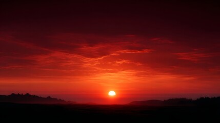 Obraz premium Vibrant sunset paints the sky with intense fiery reds and oranges illuminating dramatic clouds over a dark silhouetted landscape