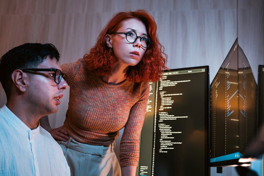 Two professionals collaborate in a modern office, analyzing code across multiple computer monitors, representing teamwork, technology, and efficient software development in a digital workspace.