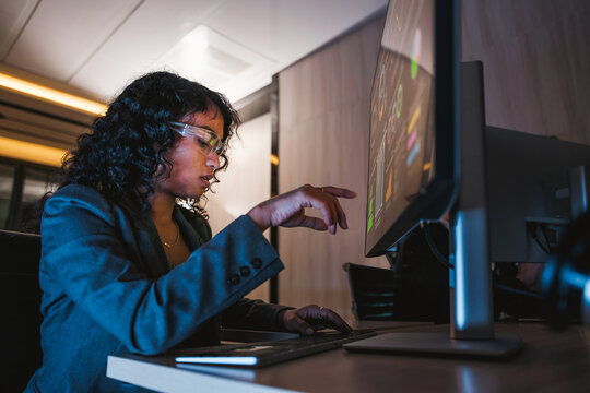 Professional woman in business attire interacts with a touchscreen monitor in a sleek modern office, engaging with digital tools for productivity, planning, and tech-enabled business operations.