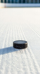 Black hockey puck on ice rink surface with clear lines  