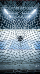 Hockey goal net with puck in empty ice rink illuminated by lights  