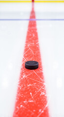Black hockey puck on red line of ice rink ready for play  