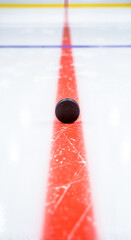 Ice hockey puck on red line of rink with clear ice background  