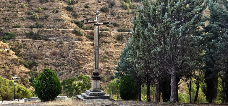 Cruz monumental rodeada de cipreses en los montes del Sacromonte, Granada, con ladera &aacute;rida al fondo. Religi&oacute;n, paisaje.