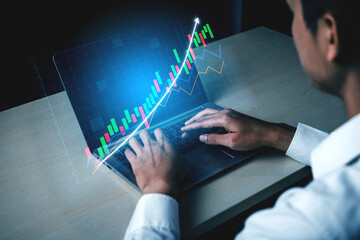 A business professional works on a laptop with financial data visualization projected above the device, showcasing market trends and analysis in a modern workspace. Impute