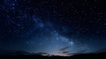 Naklejka premium Vast expanse of the Milky Way galaxy and stars across a dark clear night sky with subtle clouds near the horizon