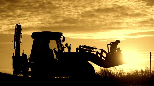 Simple rural life and works in countryside, farmer driving bulldozer in farmland . Backlit silhouette of worker riding contemporary tractor in nature, beautiful sunset or sunrise, modern equipment
