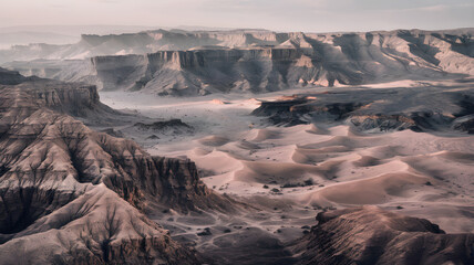 An expansive aerial view of a rugged desert landscape featuring towering canyons, eroded cliffs, and vast sandy plains under a soft, hazy sky