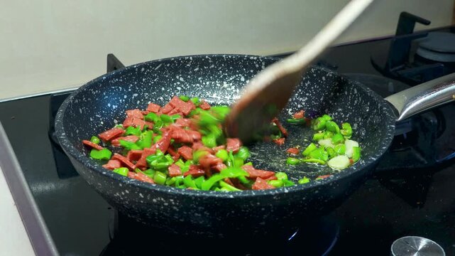 Cooking sucuklu menemen with tomatoes, peppers and Turkish sausage in a pan