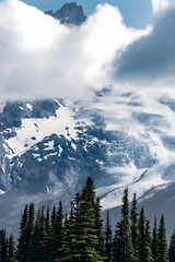 Snowcapped Mountain Peak Through Clouds Above Evergreen Forest
