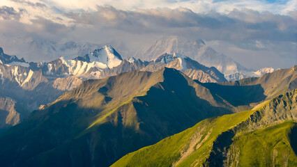 Alpine Peaks and Rolling Green Hills Under Dramatic Cloudy Skies