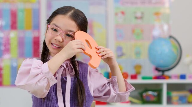 Young Student Holding Foam Number Nine in Classroom
