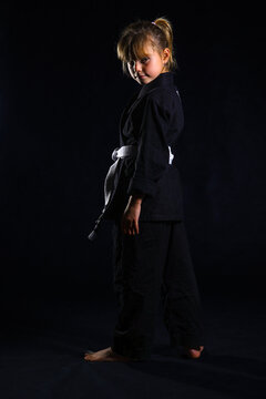 Young girl in black BJJ gi with white belt posing confidently in martial arts studio, symbolizing discipline, strength and beginner training in Brazilian Jiu-Jitsu
