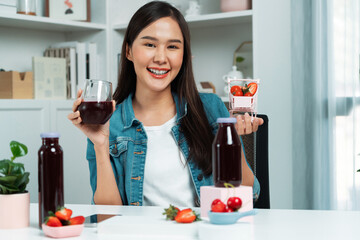 Smiling young beautiful Asian reviewing tasty mixed strawberry and cherry juice detox drinks,...