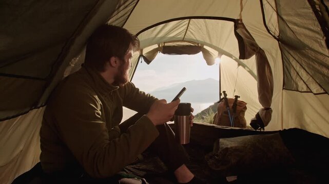 Traveler using phone map in tent early morning sunlight across fabric concept of organization direction readiness modern adventure calm mindset and thoughtful travel planning