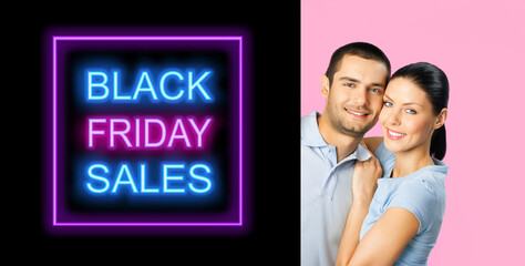 Happy smiling cute couple advertise, point sign board with ad text. Hugging boyfriend, girlfriend, isolated pink background. Brunette man, woman peeping out banner with Black Friday Sales sign text.